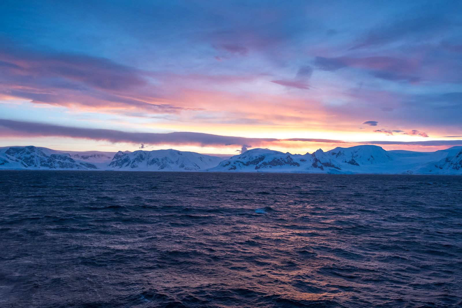 Sunset over icy mountains and calm water on the Antarctic Peninsula
